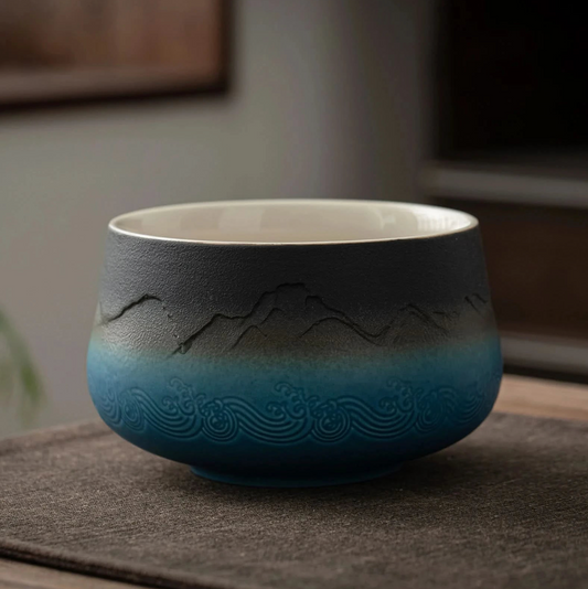 A set of matcha tea ceremony equipment laid out on a wooden table, including a ceramic bowl, bamboo whisk, bamboo scoop, ceramic whisk holder, ceramic scoop stand, cotton tea cloth, and a matcha powder sifter.