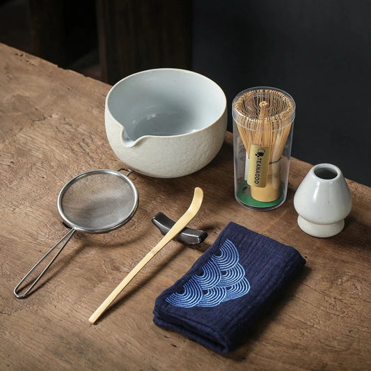 Tea-making tools including a bowl, whisk, and towel on a wooden surface.