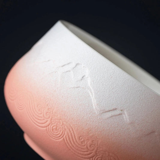 A set of matcha ceremony tools laid out on a wooden surface, including a ceramic bowl, bamboo whisk, bamboo scoop, ceramic whisk holder, ceramic scoop stand, cotton tea cloth, and a matcha powder sifter, with a pink and blue textured background.