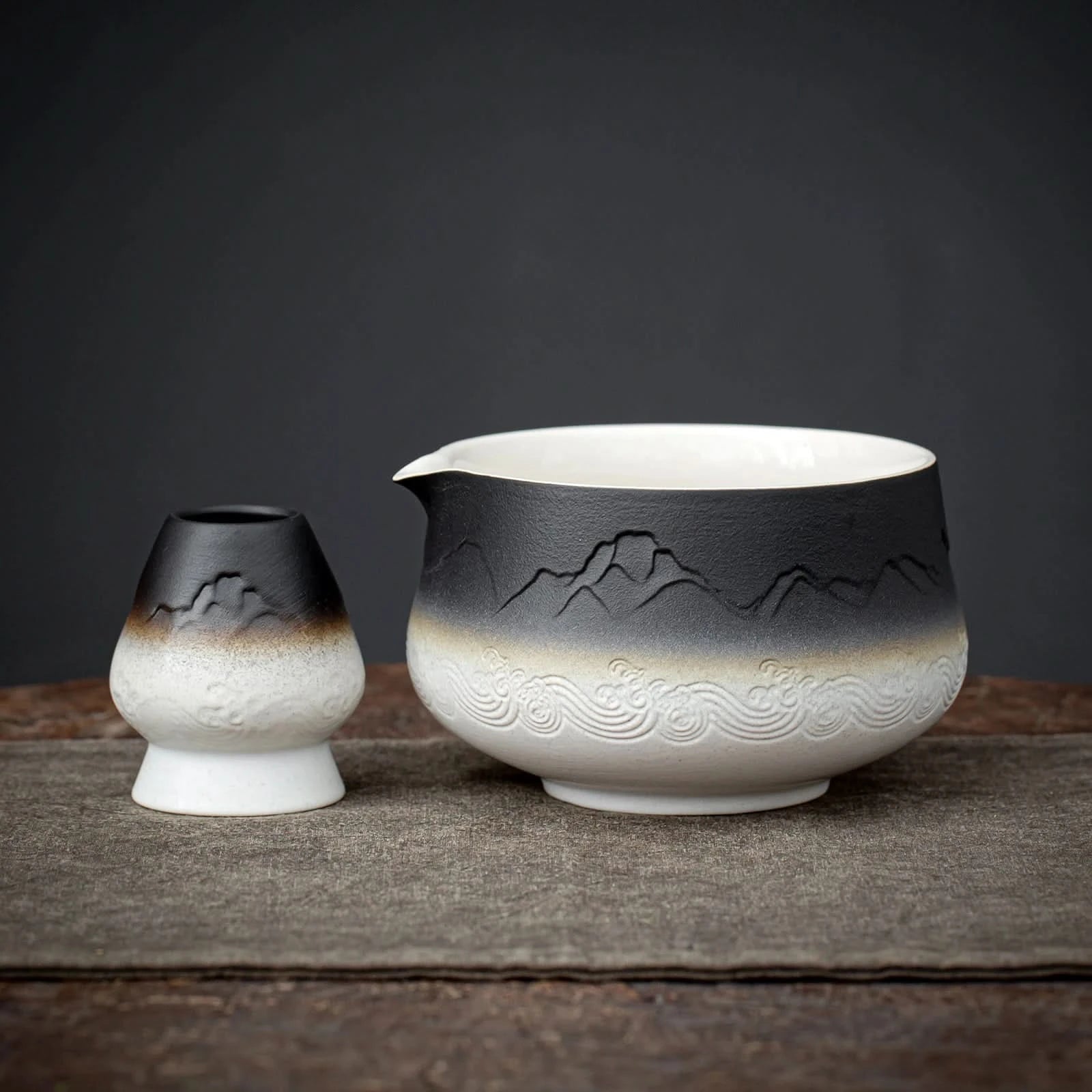 Two ceramic teapots with mountain and wave designs on a dark background