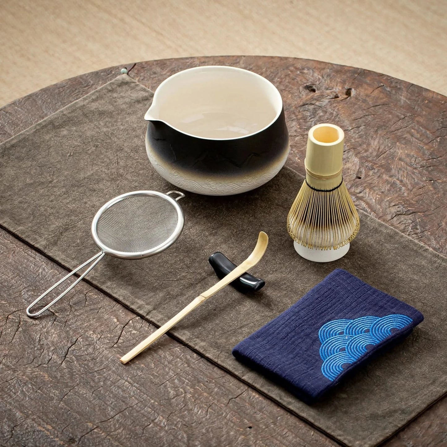 Tea-making tools including a bowl, whisk, and cloth on a wooden surface