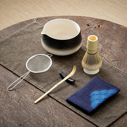Tea-making tools including a bowl, whisk, and cloth on a wooden surface