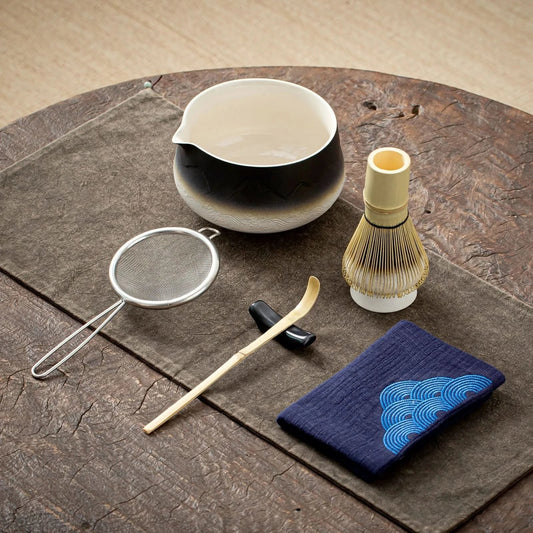 Tea-making tools including a bowl, whisk, and cloth on a wooden surface
