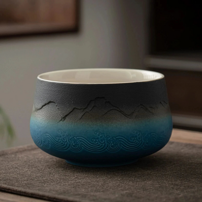 A set of matcha tea ceremony equipment laid out on a wooden table, including a ceramic bowl, bamboo whisk, bamboo scoop, ceramic whisk holder, ceramic scoop stand, cotton tea cloth, and a matcha powder sifter.