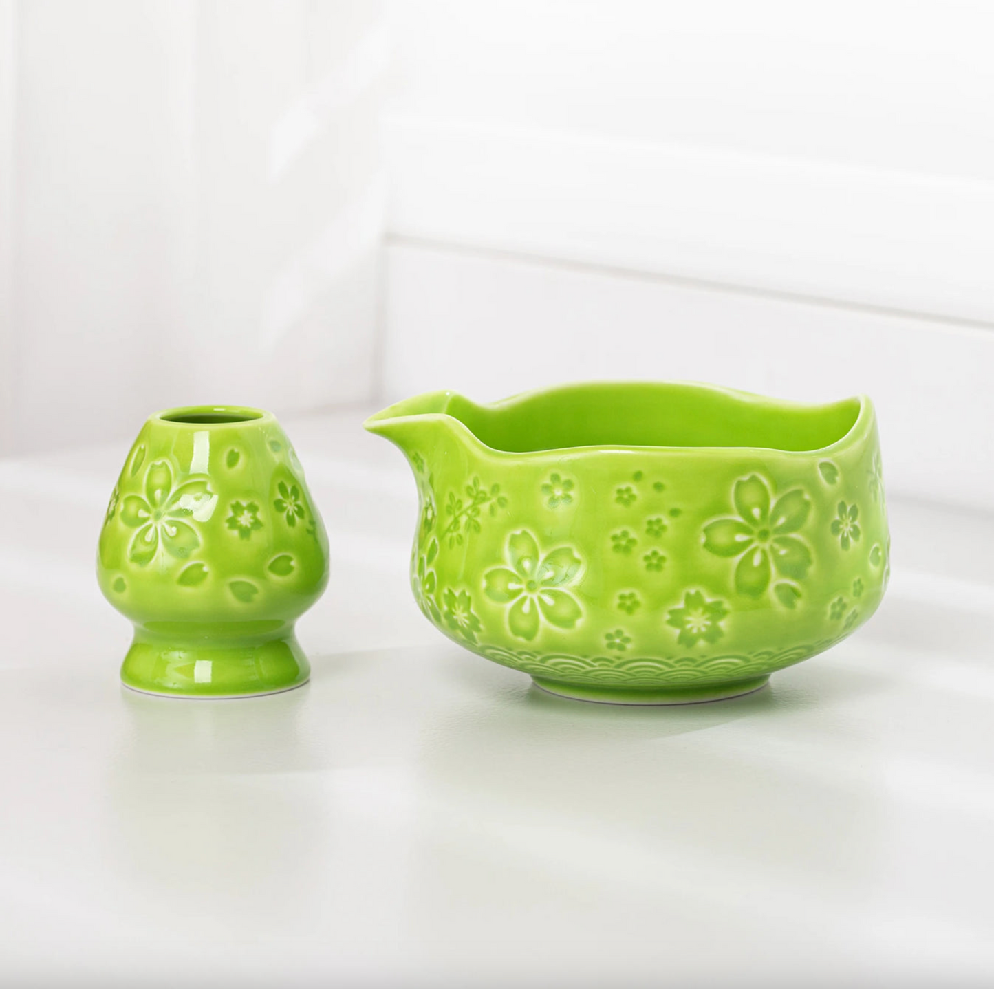 Green ceramic pitcher with floral patterns on a white background