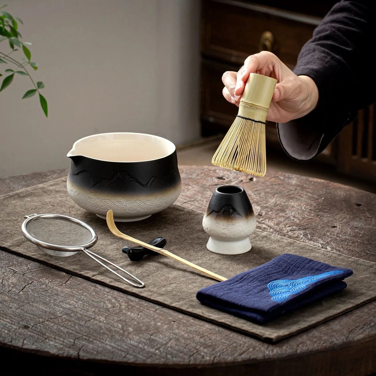 Tea-making tools including a bowl, whisk, and towel on a wooden surface.