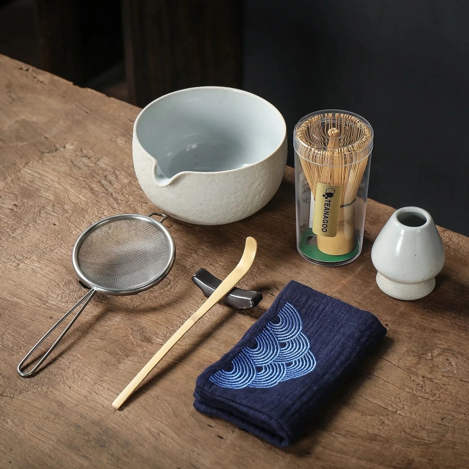 Tea-making tools including a bowl, whisk, and towel on a wooden surface.