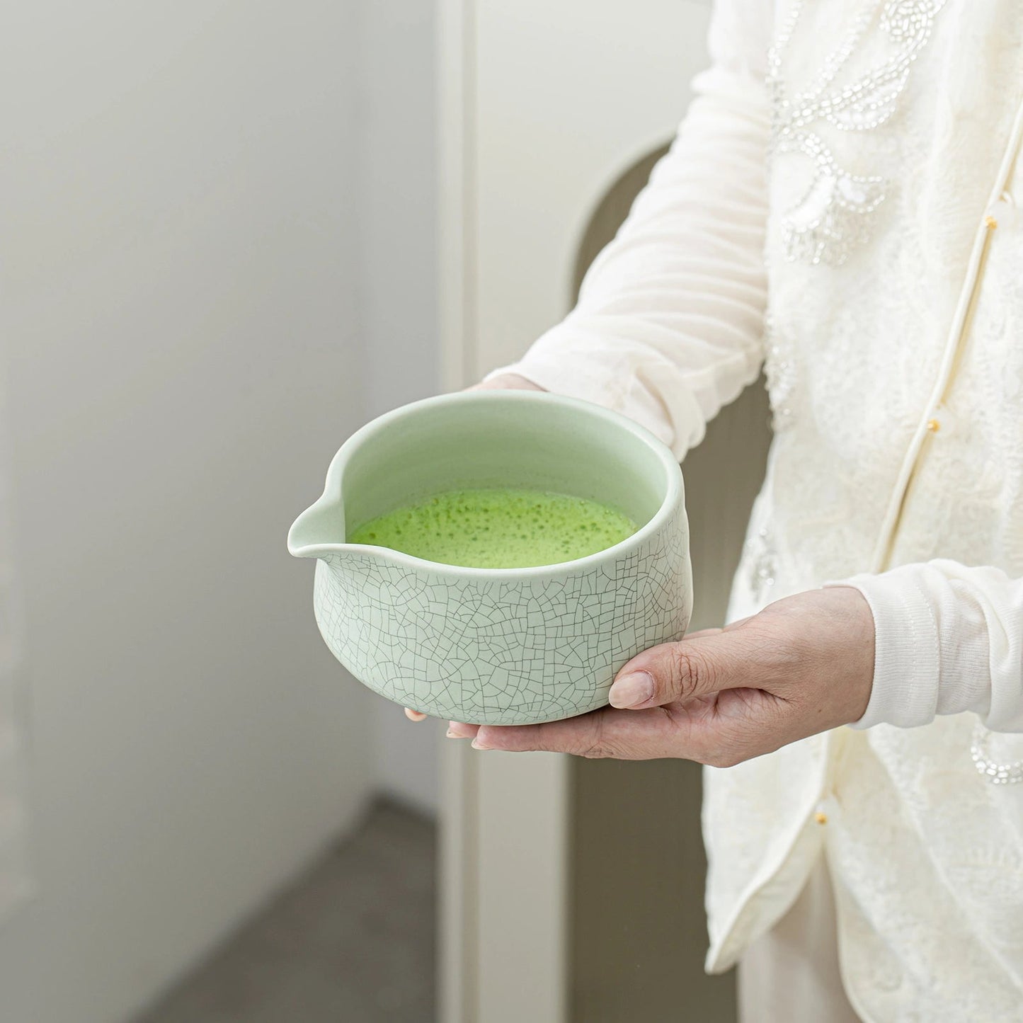 Person holding a light green ceramic bowl with green liquid against a neutral background