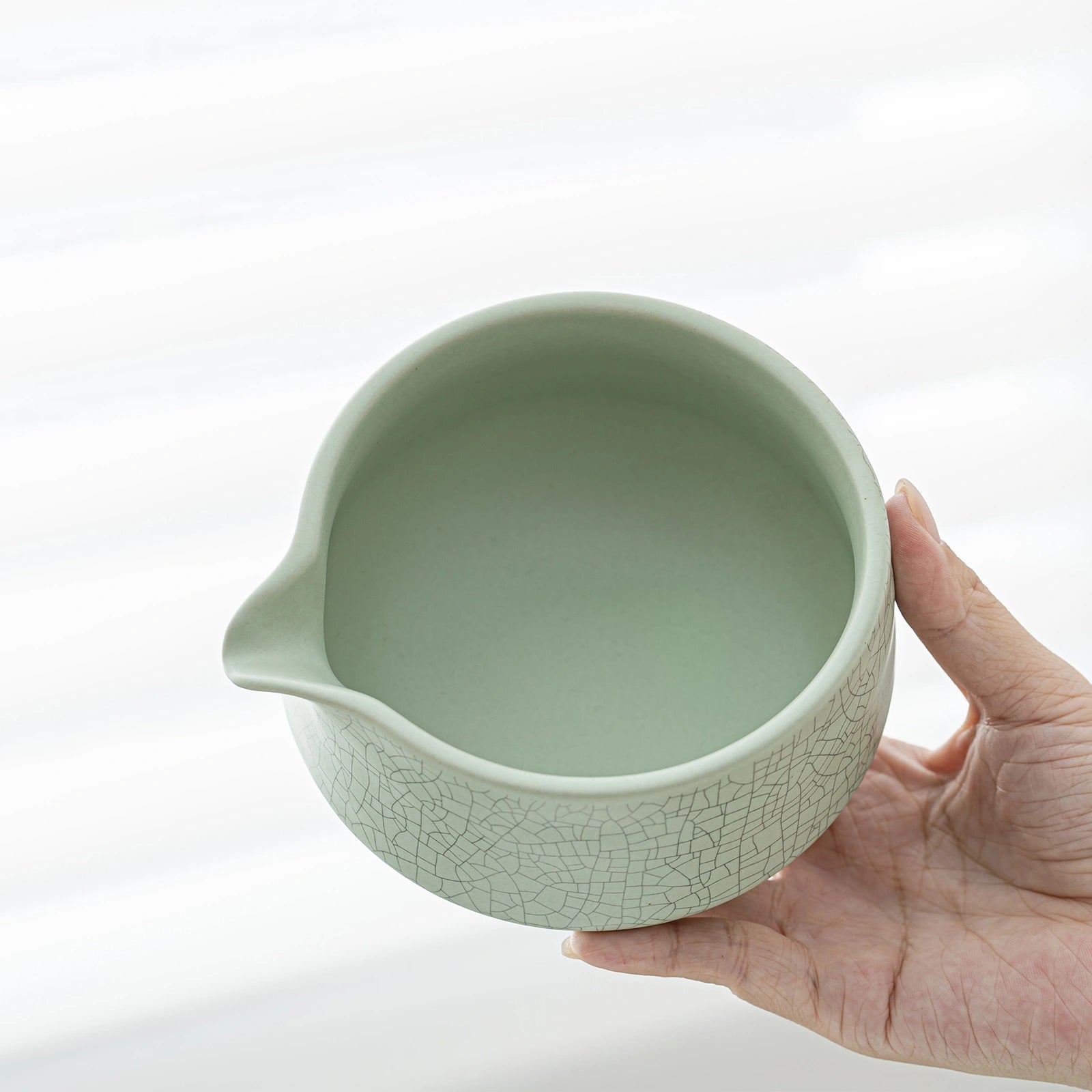 Hand holding a light green ceramic bowl with a crinkled texture on a white background
