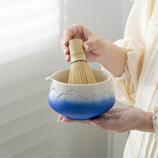 Person holding a blue and white ceramic whisking bowl with a wooden whisk.