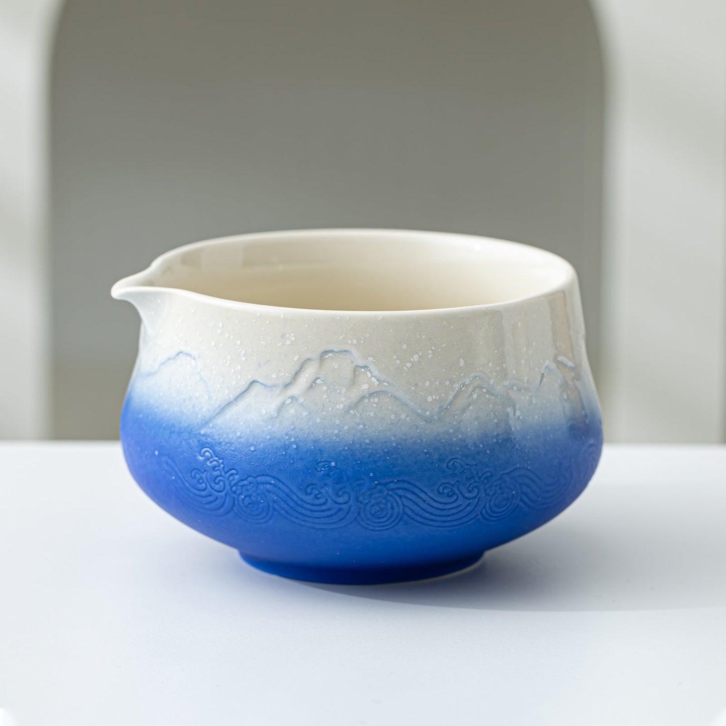 Ceramic pitcher with blue gradient and mountain design on a white surface