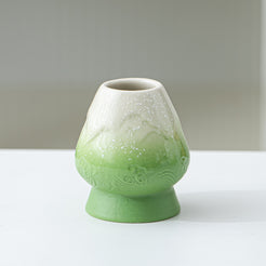 Green ceramic vase on a white surface with a gray background