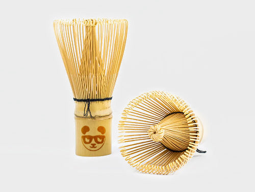A traditional Japanese bamboo whisk (Chasen) with a simple design, displayed next to its packaging that features an illustration of a panda. The whisk is light beige in color, and the packaging has a brown base with the illustration.