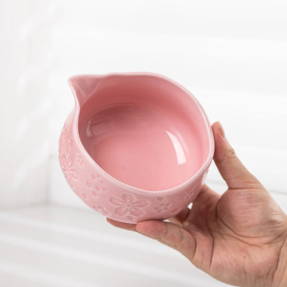 Pink ceramic pitcher held by a hand on a white background