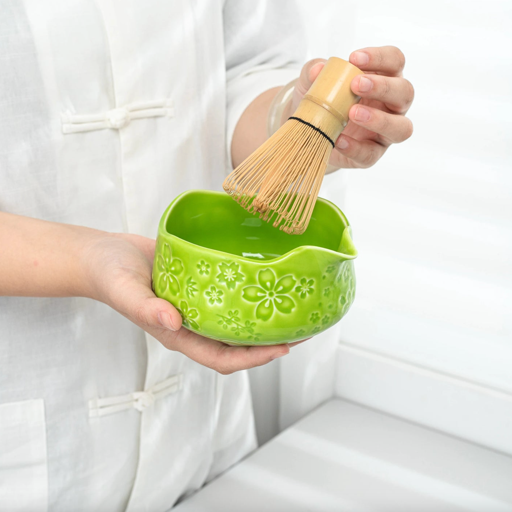 Person holding a green ceramic bowl with floral patterns and a wooden whisk.